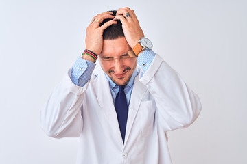 Young doctor man wearing white coat over isolated background suffering from headache desperate and stressed because pain and migraine. Hands on head.