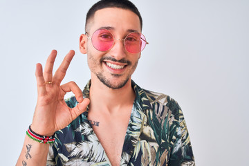 Young handsome man wearing Hawaiian sumer shirt and pink sunglasses over isolated background doing ok sign with fingers, excellent symbol