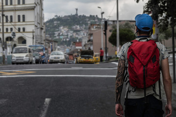 A man walking with his back turned on the road with his backpack. Behind, Pan de Azucar Mount can be seen. Quito - Ecuador