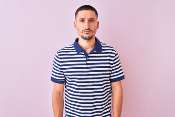 Young handsome man wearing nautical striped t-shirt over pink isolated background skeptic and...