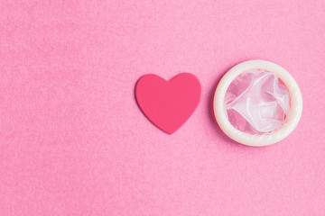 a simple flat lay about safe sex: an open condom and a pink heart on a pink background