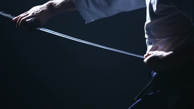 Man fighting at Aikido training with japanese sword katana in martial arts school. Healthy lifestyle and sports concept in the dark studio. Slow motion. Close up.