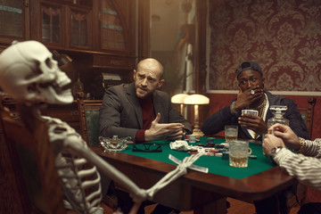 Poker players and skeleton at gaming table, fun