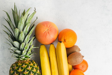Assortment of tropical fruits, banana, kiwi, orange, tangerine, lemon, pineapple, grapefruit on textured white background, top view