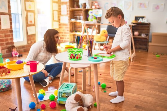 Beautiful teacher and toddler drawing using digital board around lots of toys at kindergarten