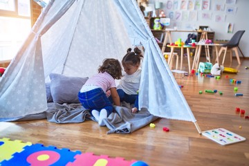Adorable toddlers lying down over blanket inside tipi smiling at kindergarten © Krakenimages.com