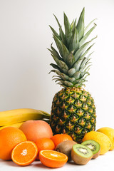 Assortment of tropical fruits, sliced and whole kiwi, orange, banana, tangerine, lemon, pineapple, grapefruit on textured white background