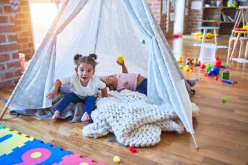 Adorable toddlers lying down over blanket inside tipi smiling at kindergarten
