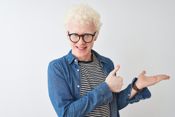 Young albino blond man wearing denim shirt and glasses over isolated white background Showing palm hand and doing ok gesture with thumbs up, smiling happy and cheerful - obrazy, fototapety, plakaty