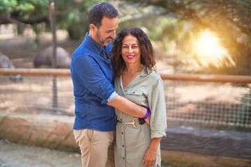 Fototapeta premium Middle age beautiful couple smiling happy and confident at town park. Standing with smile on face and hugging