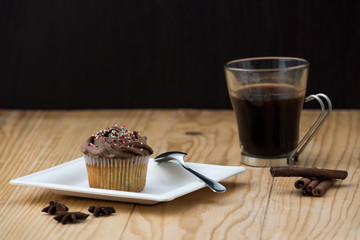 Chocolate Muffin with hot Cup of coffee, cinnamon sticks and Anise stars on a wooden table 