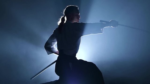 Silhouette of the master Aikido training with japanese sword katana in martial arts school. Healthy lifestyle and sports concept in the dark studio. Slow motion. Close up.