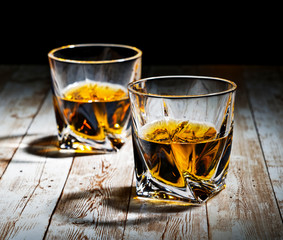 View of two filled whiskey glasses on a wooden bar top