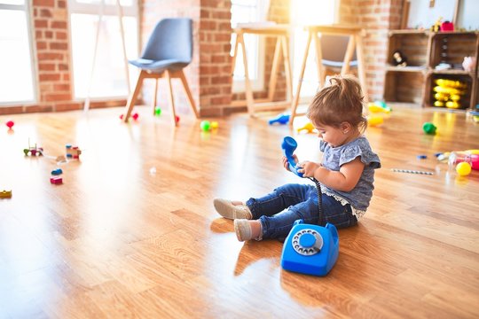 Beautiful toddler sitting on the floor playing with vintage phone at kindergarten