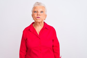 Senior grey-haired woman wearing red casual shirt standing over isolated white background puffing cheeks with funny face. Mouth inflated with air, crazy expression.