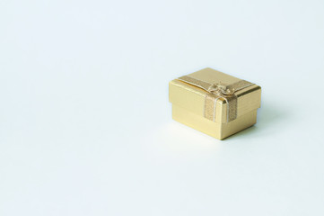 One small square golden gift box with a bow on a white background. Flat lay.