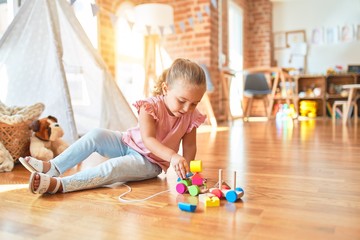 Beautiful blond toddler girl playing with train at kindergarten