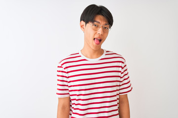 Young chinese man wearing glasses and striped t-shirt standing over isolated white background sticking tongue out happy with funny expression. Emotion concept.