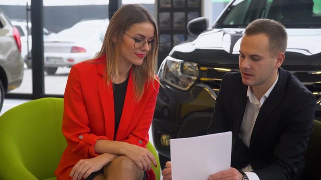 Seller and buyer are studying the contract of sale of the car. Beautiful woman buys a car