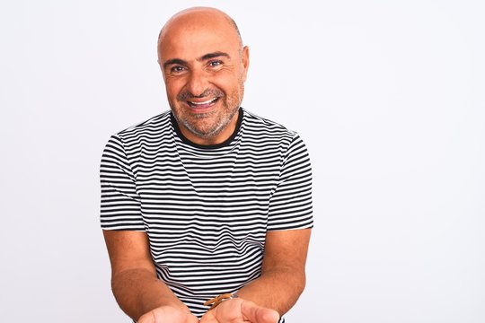 Middle age handsome man wearing striped navy t-shirt over isolated white background Smiling with hands palms together receiving or giving gesture. Hold and protection