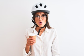 Beautiful businesswoman wearing bike helmet drinking coffee over isolated white background scared in shock with a surprise face, afraid and excited with fear expression