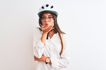 Beautiful businesswoman wearing glasses and bike helmet over isolated white background looking at the camera blowing a kiss with hand on air being lovely and sexy. Love expression.