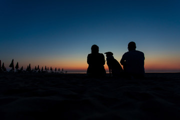 Family portrait silhouette with dog on a desert beach with closed umbrellas
