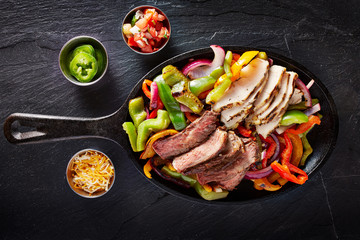aerial view of a iron skillet filled with steak and chicken mexican fajitas on slate