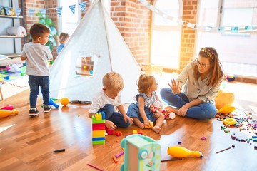 Beautiful teacher and group of toddlers playing around lots of toys at kindergarten