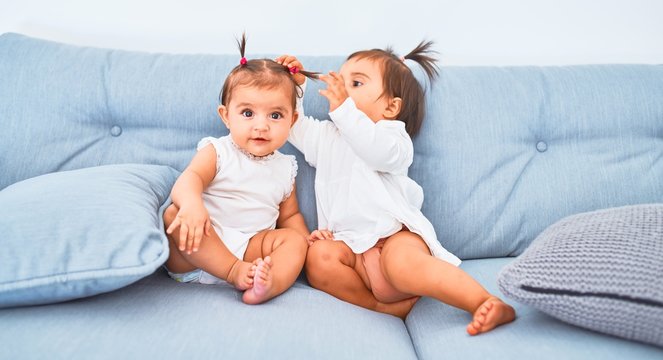 Beautiful infant happy girls playing together at home kindergarten sitting on the sofa