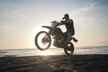 Obraz na płótnie Canvas Man on the motorbike mke jump on the black sand beach against sun