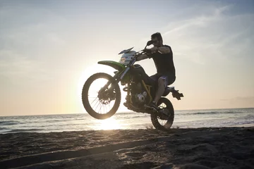 Fotobehang Man on the motorbike mke jump on the black sand beach against sun © Photo-maxx