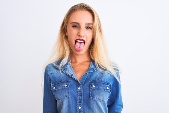 Young beautiful woman wearing casual denim shirt standing over isolated white background sticking tongue out happy with funny expression. Emotion concept.