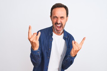 Middle age handsome man wearing blue denim shirt standing over isolated white background shouting with crazy expression doing rock symbol with hands up. Music star. Heavy music concept.
