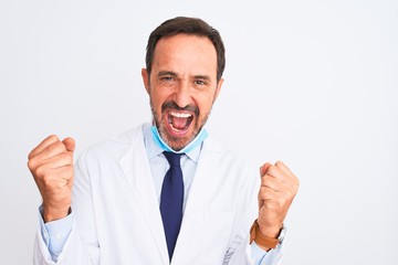 Middle age scientist man wearing coat and medical mask over isolated white background celebrating surprised and amazed for success with arms raised and open eyes. Winner concept.