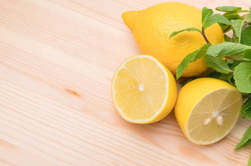 Lemon and fresh mint leaves on a natural wooden background. Mint and lemon for dessert and drinks. Yellow sliced lemon on wooden board with copy space.