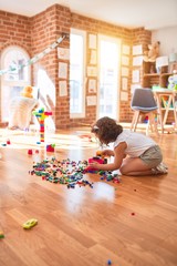 Beautiful toddler wearing glasses and unicorn diadem playing with tractor and building blocks at kindergarten