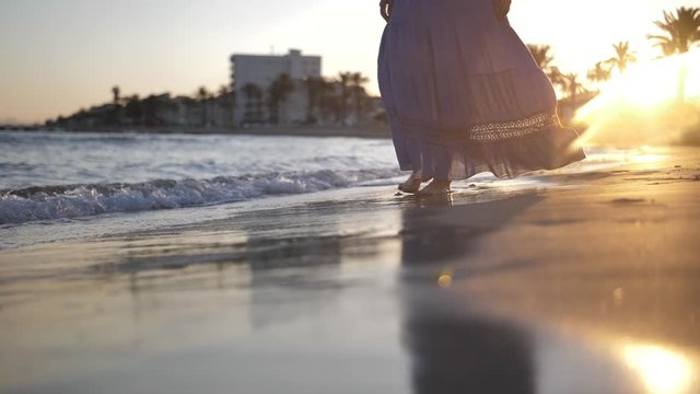 alone woman in a skirt walks along the coastline in windy weather at sunset, skirt develops in the wind, slow motion