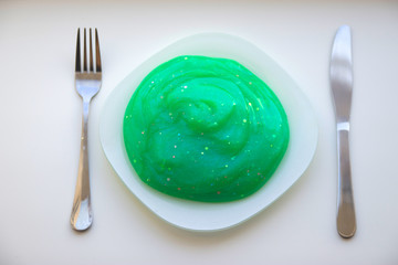 Green viscous liquid with glitter on a white plate with a knife and a fork on the sides on a white background top view