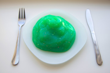 Green viscous liquid with glitter on a white plate with a knife and a fork on the sides on a white background top view