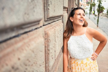 Fototapeta premium Beautiful girl leaning on the wall, young friendly woman smiling happy on a sunny day of summer