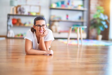 Young beautiful teacher wearing glasses lying down on the floor at kindergarten