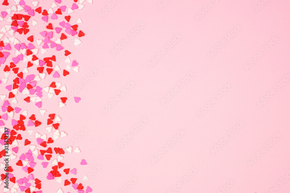 Poster valentines day side border with candy heart sprinkles over a pink textured background. copy space.
