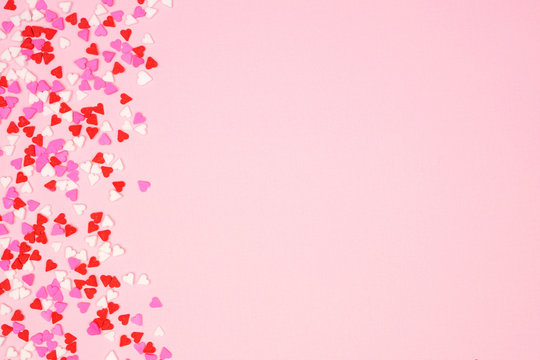 Valentines Day side border with candy heart sprinkles over a pink textured background. Copy space.