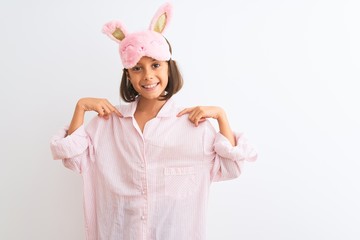 Beautiful child girl wearing sleep mask and pajama standing over isolated white background looking confident with smile on face, pointing oneself with fingers proud and happy.