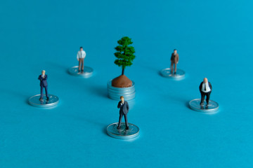 Miniature business concept - group of businessmen stand around the coin stack thinking revenue stream