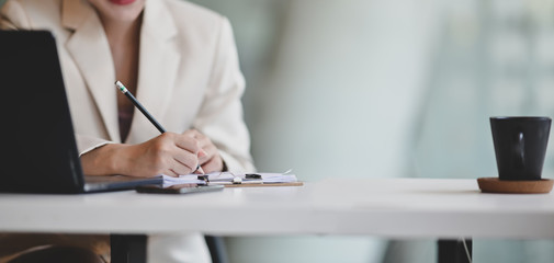 Cropped shot of professional businesswoman working on her project while writing information on documents