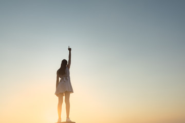 Strong, victorious and motivated young woman raising her fist up to the sunset sky.