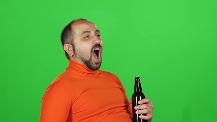 Caucasian man holds a bottle of beer in his hands and drinks with pleasure, green screen. Slow motion