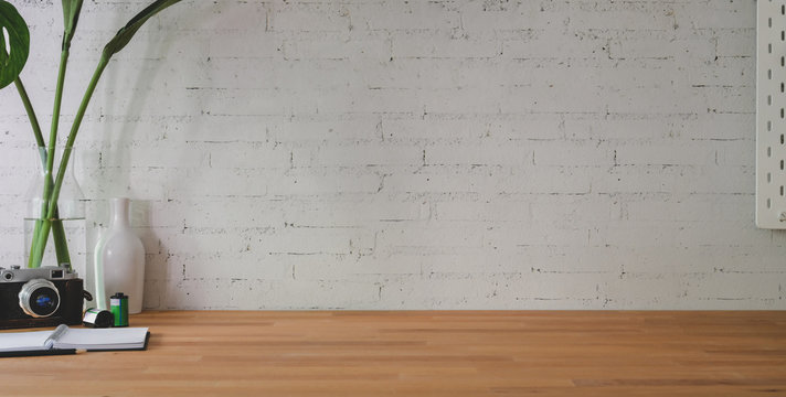 Cropped shot of comfortable workplace with camera and office supplies on wooden table and brick wall